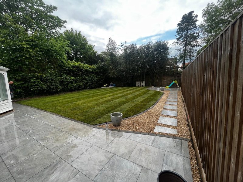 A striped lawn with stone stepping stones leading to a porcelain patio